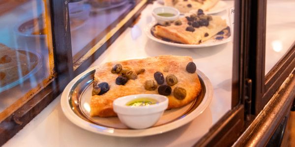 Focaccia-Stücke mit Oliven und Dip auf Tellern.