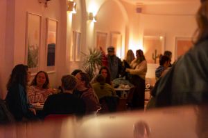 Menschengruppen sitzen an Tischen und unterhalten sich in warmem Raumlicht.