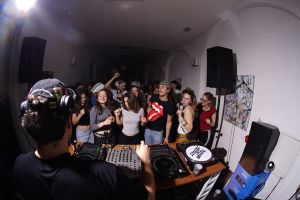 DJ über die Schulter fotografiert, Blick auf feiernde Gäste und Lautsprecher.