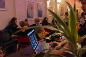 DJ-Setup mit Laptop im Anschnitt, im Hintergrund Gäste in beleuchtetem Raum.