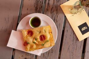 Draufsicht auf ein Stück Focaccia mit Kirschtomaten und Kräutern auf einem Teller, serviert mit grünem Dip, einer Serviette und der Speisekarte des Cafés "JOS FRITZ".