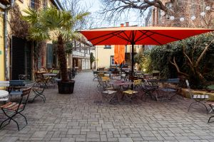 Innenhof mit großem orangefarbenem Sonnenschirm, Palme und Tischen.