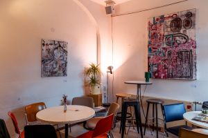 Sitzecke mit abstrakten Gemälden, Stehlampe und bunten Stühlen.