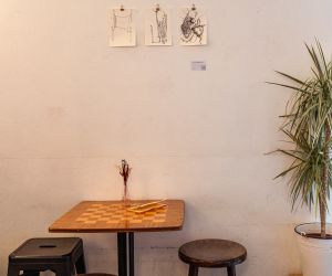 Schachtisch aus Holz mit zwei Hockern vor weißer Wand mit Skizzen.