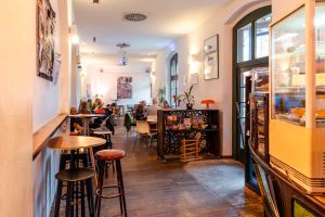 Café-Innenraum mit Gästen an Tischen, Holzboden und Wandkunst.