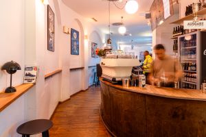 Barista in Bewegung hinter geschwungener Holztheke mit Espressomaschine.