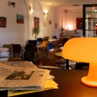 Eine leuchtende orangefarbene Retro-Tischlampe in Pilzform steht auf einem Tresen neben einer Tageszeitung.