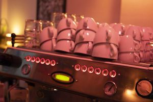 Espressomaschine mit gestapelten weißen Tassen in warmem Licht.