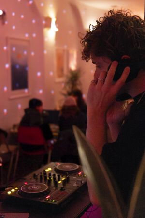 DJ mit Kopfhörern im Profil vor einer Wand mit Lichtreflexen.