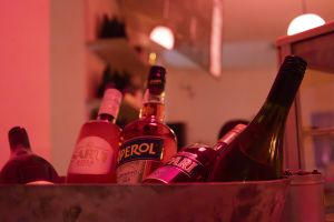 Flaschen von Sarti, Aperol und Campari in einer Schale bei roter Beleuchtung.