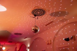 Diskokugel an der Decke, die Lichtmuster in einem rötlich beleuchteten Raum wirft.